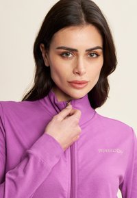 Giacca zip-up viola con maniche lunghe, tessuto morbido e colletto alto. Presenta un accento con logo in strass sul petto.