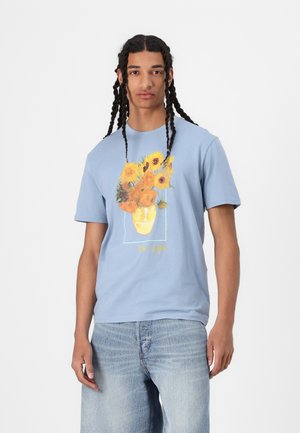 Light blue cotton t-shirt featuring a graphic of sunflowers in a vase. The design includes pastel accents and "Van Gogh" text.