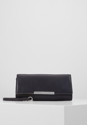 Black rectangular leather clutch bag with wrist strap and silver metal clasp on white pedestal against gray background.