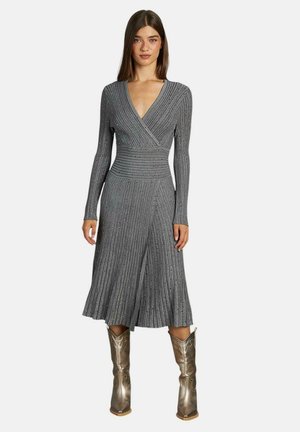 Vestido gris de manga larga con diseño cruzado y dobladillo acampanado, combinado con botas altas plateadas de metal. No se observan patrones ni acentos visibles.