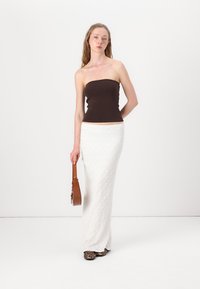 Brun strapless topp parat med en lång vit strukturerad kjol; håller en brun handväska. Skorna har ett leopardmönstrat design.