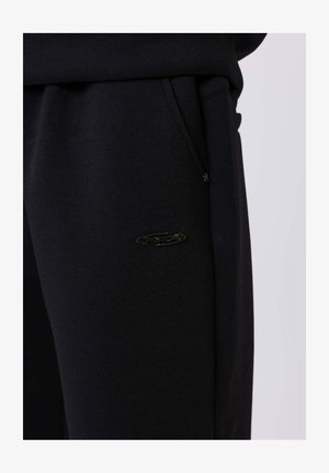 Zwarte sweatpants gemaakt van een zacht materiaal, voorzien van een zijzak, een elastische tailleband en een klein zwart logo op de dij.