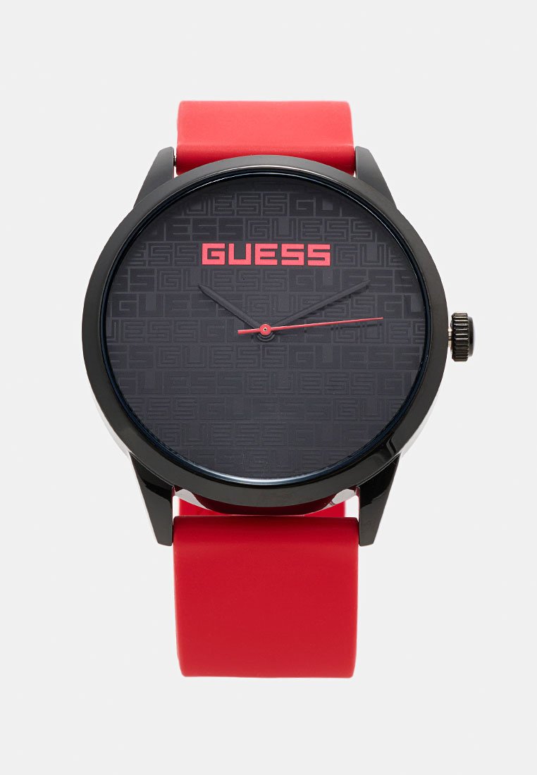 Reloj analógico negro con correa de goma roja. La esfera negra texturizada presenta un patrón de logo en relieve y el nombre de la marca en rojo "GUESS". Marcadores de hora plateados.