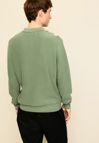 Groene geribbelde gebreide trui met een kraag, lange mouwen en contrasterende schouderdetails. Slim fit, zachte textuur en elastische boorden aan mouwen en zoom.