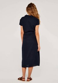 Marineblaues Leinenkleid mit kurzen Ärmeln, Kragen, tailliertem Schnitt und Midi-Länge. Verfügt über einen seitlichen Schlitz und wird mit braunen Sandalen kombiniert.