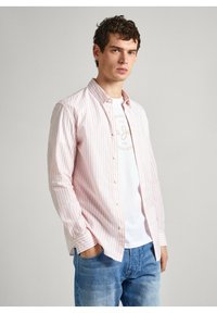 Lichtroze en witte gestreepte overhemd met lange mouwen, met knopen en een kraag, gedragen over een wit T-shirt. Gecombineerd met lichtblauwe denim jeans.