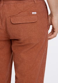 Bruine lichtgewicht broeken met een gestructureerde stof. Voorzien van een achterzak met een klep en een merklabel. Casual pasvorm.