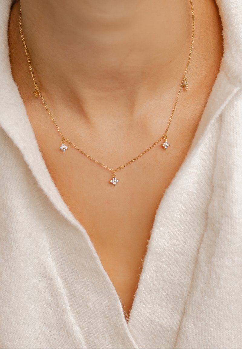 Collier délicat en chaîne d'or avec trois petits groupes de diamants porté autour du cou d'une femme, associé à un vêtement blanc doux à col en V.
