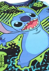 T-shirt en coton bleu présentant un personnage de dessin animé aux grands yeux et à la bouche ouverte, sur un fond graphique noir et vert néon.