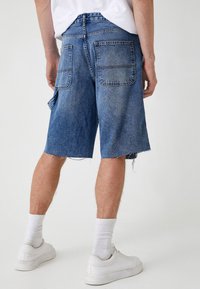 Pantalones cortos de denim con un dobladillo deshilachado, lavado azul claro, dos bolsillos traseros y un ajuste relajado, combinados con zapatillas blancas y calcetines hasta la pantorrilla.