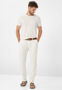 Pantaloni di lino bianchi, t-shirt beige chiaro, cintura in pelle marrone e sandali marroni. Texture liscia, vestibilità comoda e design minimale.