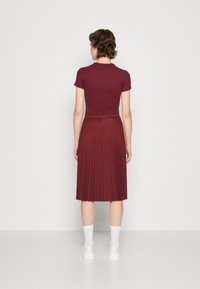 Top rigato borgogna abbinato a una gonna plissettata. La gonna presenta una texture liscia, mentre il top ha maniche corte e un design aderente. Calze bianche e sneakers.