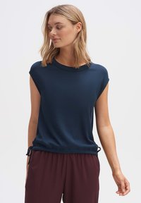 Top in maglia a costine blu navy con collo alto, maniche corte e laccetti laterali regolabili, abbinato a pantaloni larghi bordeaux.