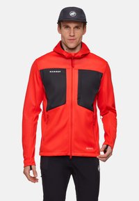 Rød softshell-jakke med sorte accenter, lynlås-lommer og justerbar hætte. Lavet af letvægtsmateriale til udendørs aktiviteter.
