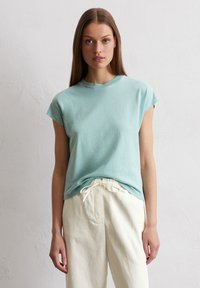Hellblaues T-Shirt mit kurzen Ärmeln, rundem Halsausschnitt, entspannter Passform und glatter Textur, kombiniert mit cremefarbenen Jogginghosen mit Kordelzug.