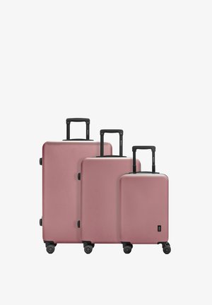 Tre valigie rigide rosa di diverse dimensioni, con maniglie nere retrattili e ruote. Superficie liscia e design minimalista.