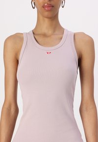 Lys rosa tanktopp med ribbet tekstur, med rund halslinning og en liten rød logo detalj foran i midten.