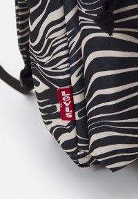 Svart och gräddfärgad zebrarandig ryggsäck gjord av hållbart tyg, med en röd Levi's-logotyp som är tydligt synlig.