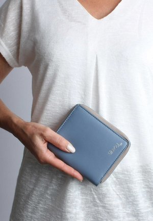 Light blue wallet made of smooth leather with a beige accent. Features rounded corners and stitched edges. Held in a hand against a white backdrop.