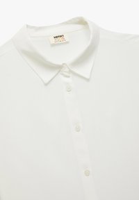 Vit kortärmad polo tröja i bomull, med klassisk krage och femknapplist. Mjuk textur och slät finish.