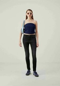 Jeans de lavagem escura com uma silhueta ajustada, combinados com um top tom de azul-marinho sem alças. Os acessórios incluem uma bolsa de ombro azul-claro e óculos de sol brancos.