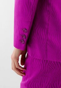 Traje fucsia con una sutil textura de estampado de cebra. Presenta un puño con tres botones a juego y una silueta elegante y entallada.