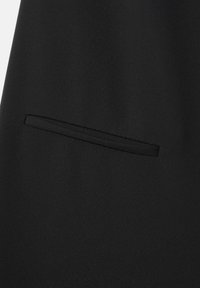 Tejido negro con una textura suave. Presenta un bolsillo estrecho y elegante integrado en el diseño, lo que contribuye a un aspecto minimalista.