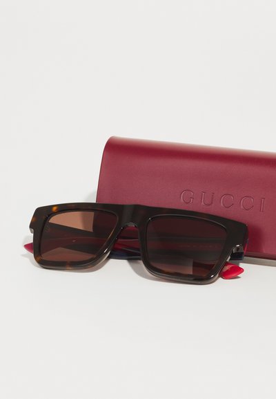 Bruna sköldpaddsmönstrade solglasögon med överdimensionerade fyrkantiga linser, med en stilren design. Åtföljas av ett vinrött skyddande fodral präglat med "GUCCI."
