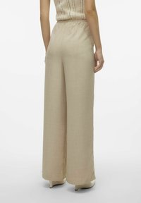 Pantalons larges beiges en tissu léger, dotés d'une taille haute élastique, d'une texture lisse et d'un design fluide.