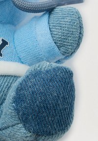 Detailní záběr modrých pletených dětských ponožek s texturovanou podrážkou připomínající denim na bílém pozadí.