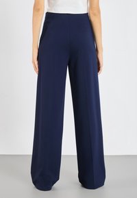 Navy wide-leg trousers made of smooth fabric, featuring a high waistband, minimal seams, and a flowing silhouette that falls to the floor.
