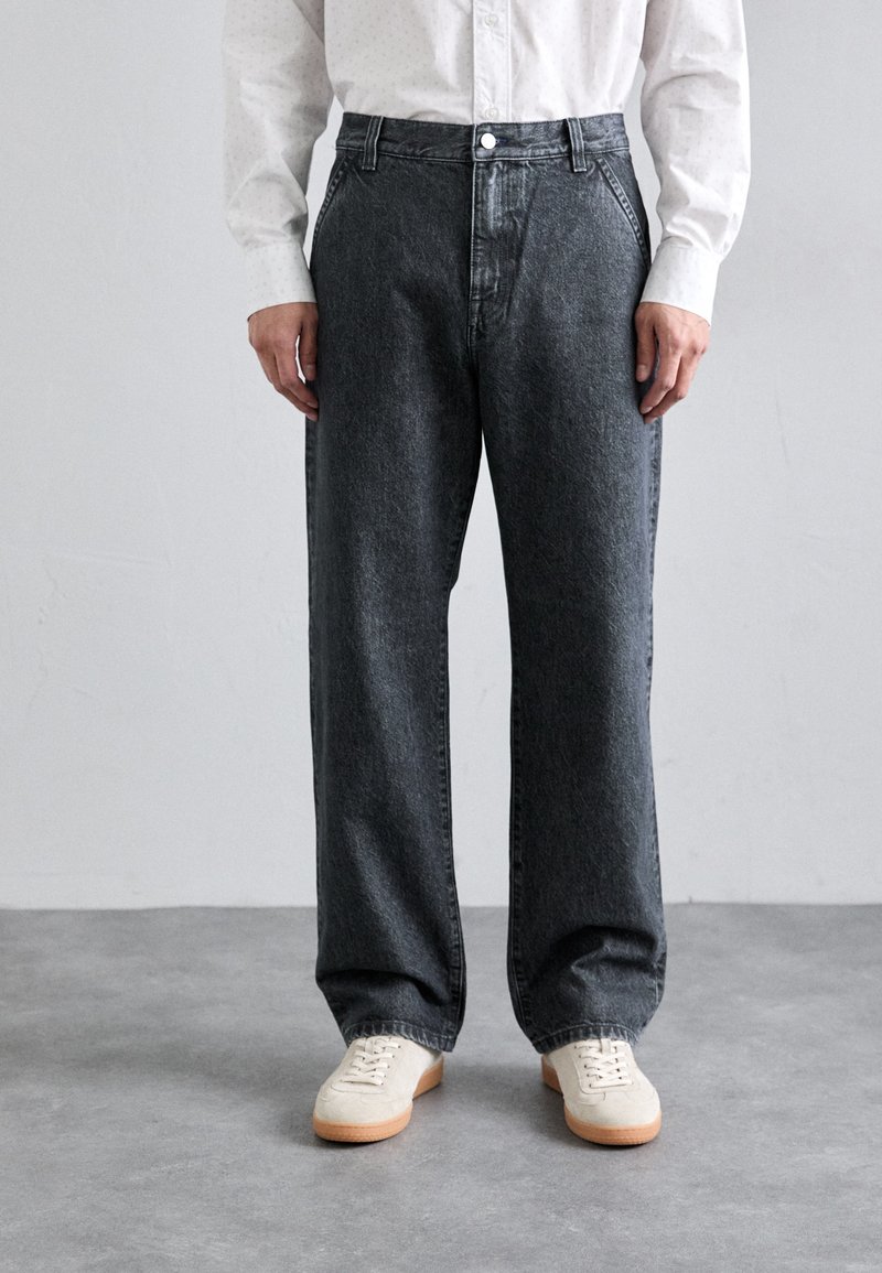 Mörkgrå vida jeans med hög midja, med knappgylf och sidofickor, kompletterade med krämfärgade sneakers.