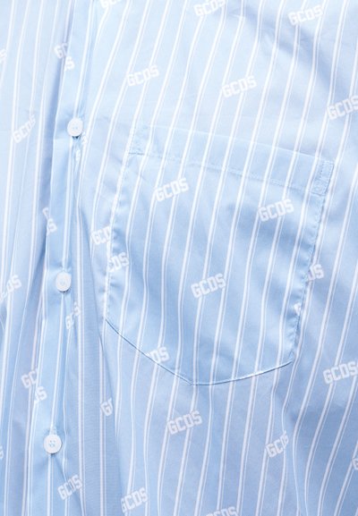 Gaiši zila pogājama krekla ar baltām vertikālām svītrām un krūšu kabatu, ar mazu atkārtotu "GCDS" teksta rakstu.