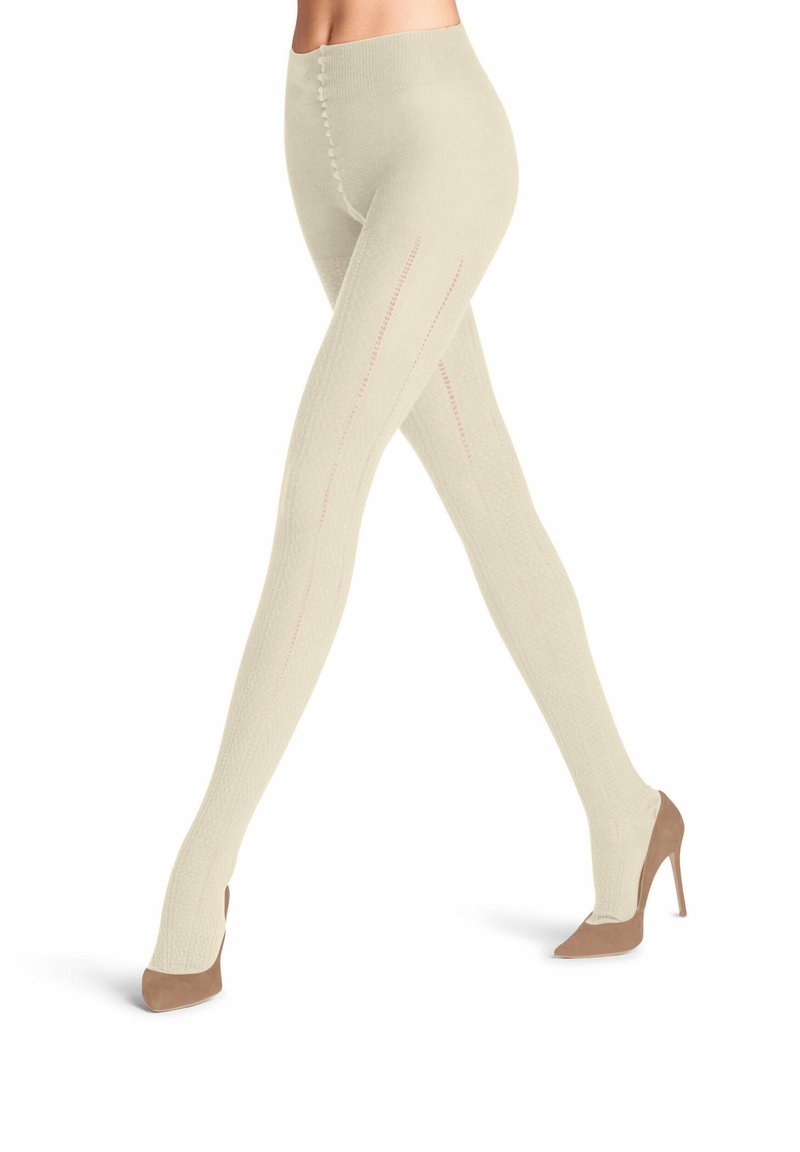 Collants jusqu'aux genoux en maille beige clair, avec des côtes verticales et de subtils détails de couture rose. Portés avec des talons en taupe.