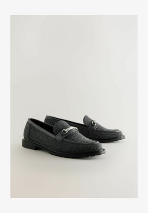 Grå filtsko med en sort gummisål. En dekorativ rem med sølvhardware tværs over toppen. Glatte læderdetaljer ved hælen.