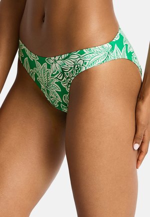 Zielony dół bikini z białymi wzorami kwiatów i liści, noszony przez osobę o średnio ciemnej karnacji, ręka spoczywa na górnej części uda.