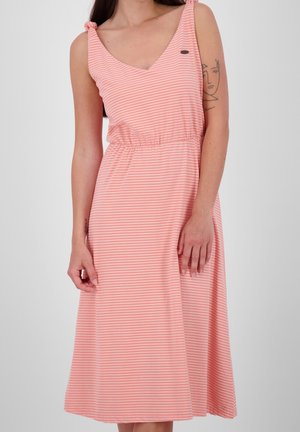 Kvinde iført en ærmeløs, lyserød og hvidstribet midikjole med bindebånd på skuldrene og en rynket talje, der viser en tatovering på sin arm.