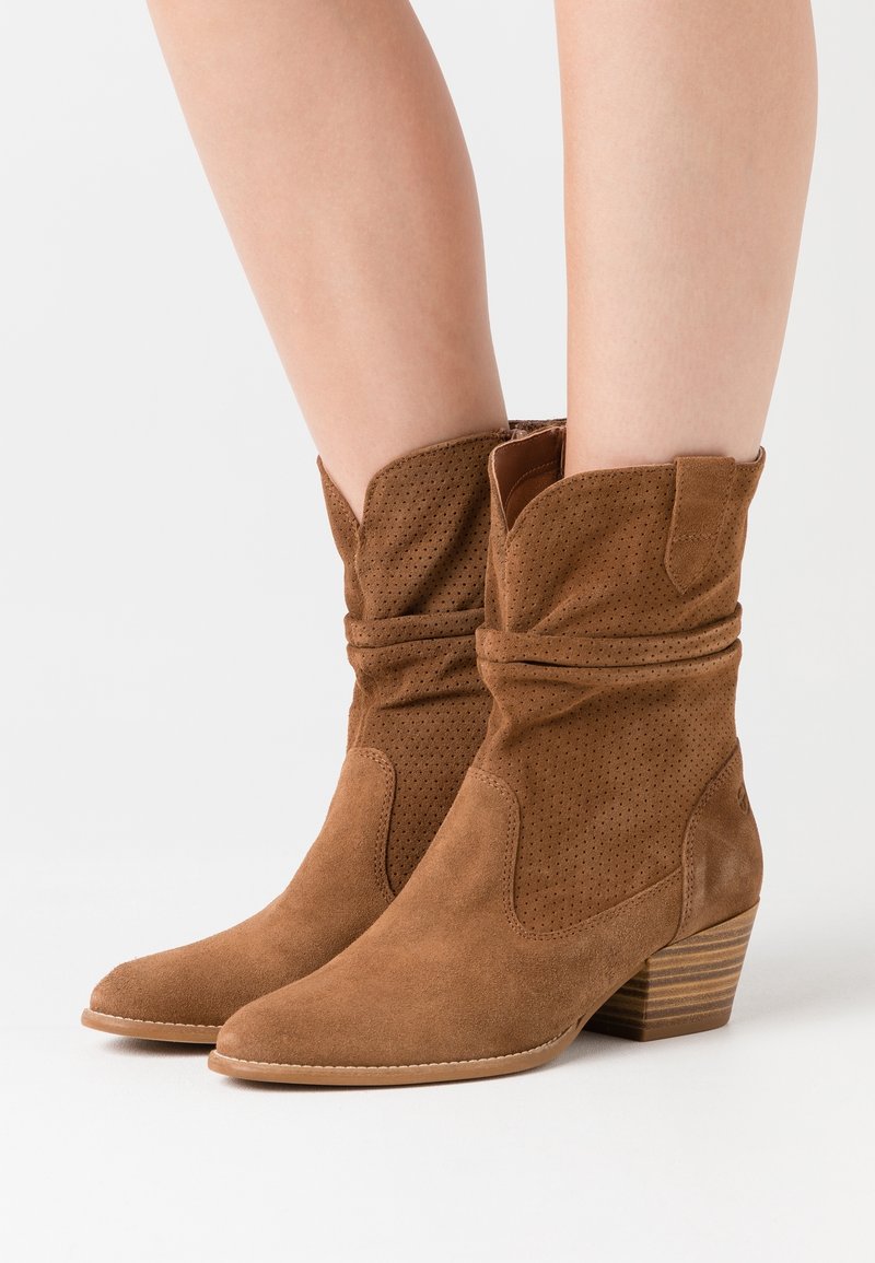 Bruna mockaankelboots med slapp design, spetsig tå, perforerade detaljer och en staplad klack med texturerad finish.