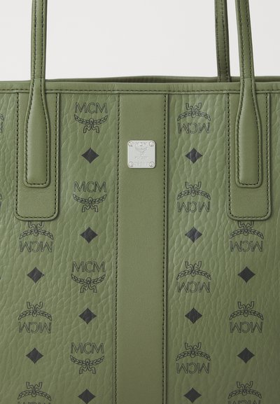 Zielona skórzana torba tote o teksturowanym wykończeniu, z czarnymi logo MCM i diamentowymi wzorami. Zawiera srebrną tabliczkę z logo oraz mocne uchwyty.