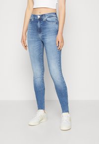 Ljust blå skinny jeans med en urblekt design, hög midja, fem fickor och en metallknappstängning, ihop med vita sneakers.