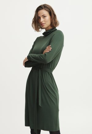 Grön, långärmad klänning i ett mjukt, stretchigt tyg. Har en hög döljkrage och ett knytbart midjebälte för form.