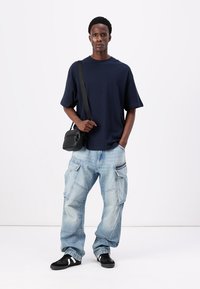 Ναυτικό κοντομάνικο πουκάμισο, ανοιχτό μπλε φαρδιά cargo τζιν με τσέπες και μαύρα αθλητικά παπούτσια, συμπληρωμένα με μια μικρή μαύρη τσάντα σώματος.