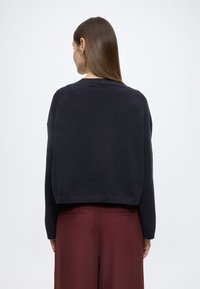 Camisola cropped azul-marinho escura, feita de tecido de malha macio, com decote redondo e bainha canelada, combinada com calças largas de perna larga cor borgonha.