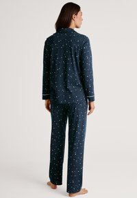 Marineblauw pyjama set met een wit sterrenpatroon, bestaande uit een lange mouwen en broek, gemaakt van zachte stof, met contrasterende witte bies langs de mouwen.
