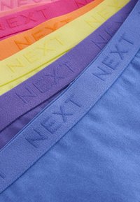 Fasce di tessuto colorato in rosa, arancione, giallo, viola e blu con il branding in rilievo "NEXT" lungo il bordo superiore. Texture morbida, tonalità variabili.
