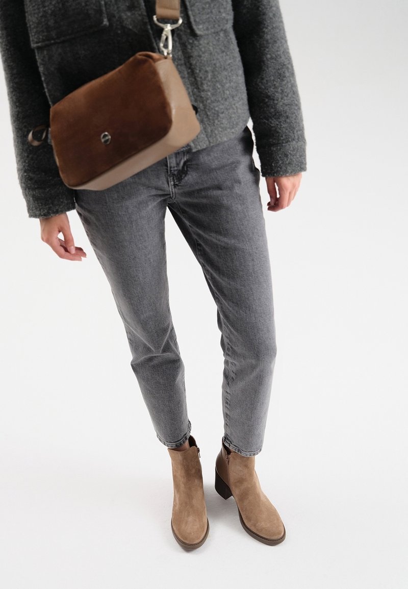 Personne portant un jean gris, des bottines en daim marron à talons, une veste en laine grise et un sac bandoulière marron.