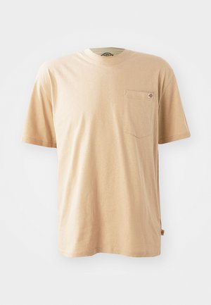 Beige cotton t-shirt with short sleeves, round neckline, and a left chest pocket. Features a small logo tag on the pocket.