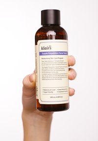 Bouteille de toner en plastique ambré foncé avec un bouchon noir à vis. Contient 180 mL. L'étiquette affiche les informations sur le produit en texte noir et violet.