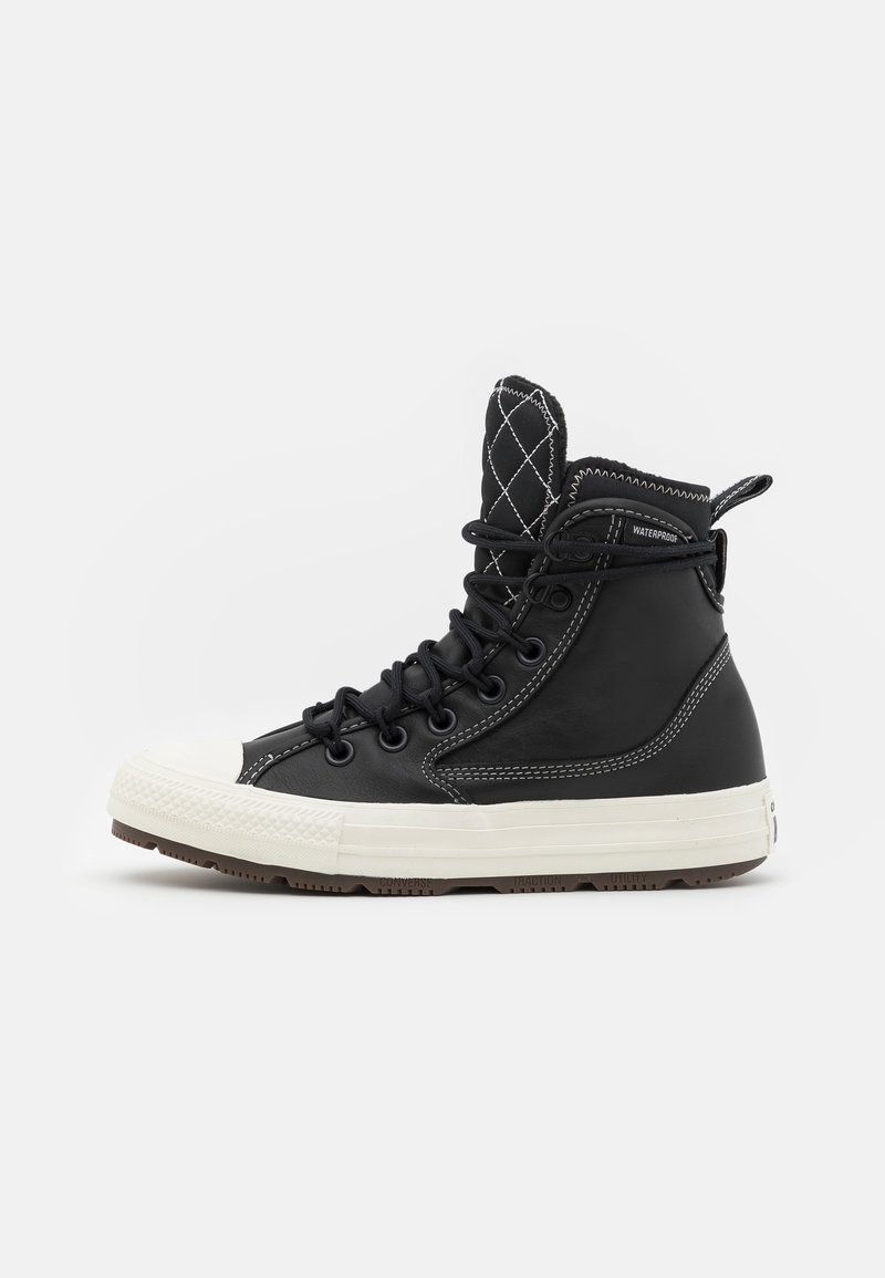 Bottine de sneaker haute imperméable noire avec semelle en caoutchouc blanche, coutures contrastées, languette matelassée et lacets noirs, vue de profil.