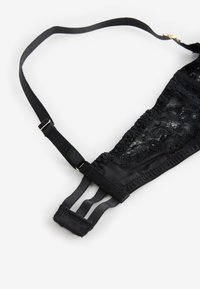 Fekete csipkés melltartópánt állítható fém csúszkákkal és három szálas elasztikus szalaggal fehér háttéren.